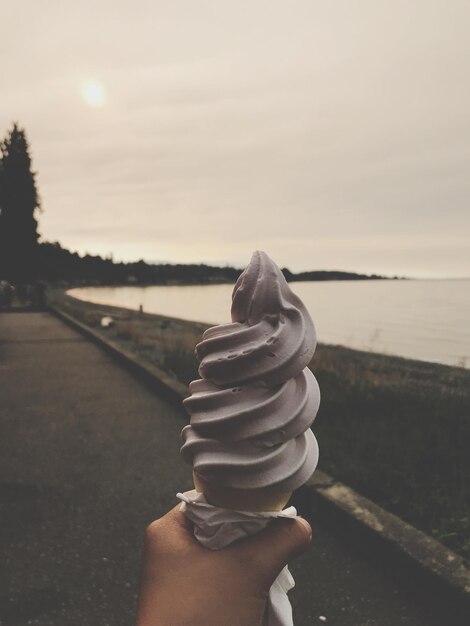 Photo cropped hand holding ice cream by sea on footpath