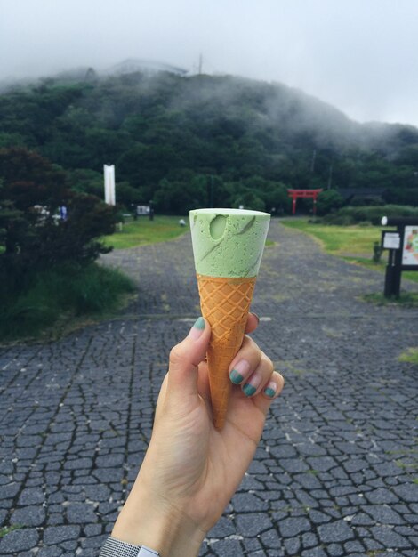 Cropped hand holding ice cream cone against mountain