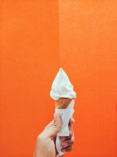 Photo cropped hand holding ice cream cone against orange wall