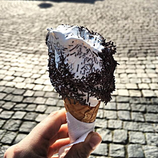 Photo cropped hand holding ice cream cone on footpath