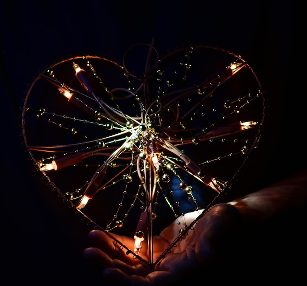Foto mano tagliata che tiene una forma di cuore illuminata in camera oscura