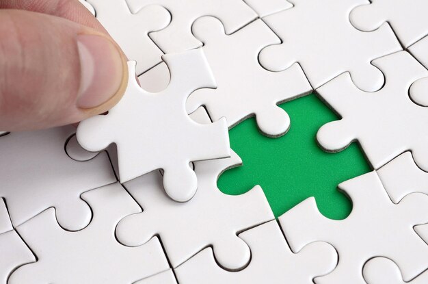 Foto mano tagliata che tiene un pezzo di puzzle su un puzzle