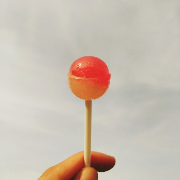 Foto mano tagliata che tiene un lecca-lecca contro il cielo