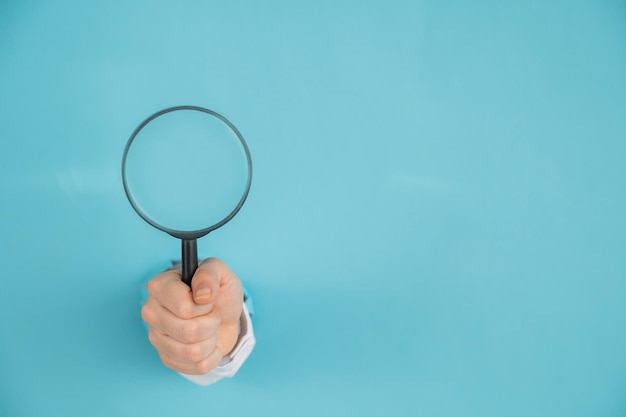 Photo cropped hand holding magnifying glass against blue background