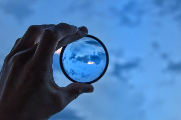 Foto mano tagliata che tiene una lente d'ingrandimento contro il cielo blu