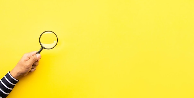 Photo cropped hand holding magnifying glass against yellow background