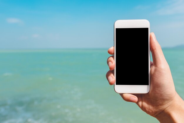 Foto mano tagliata che tiene il cellulare contro il mare