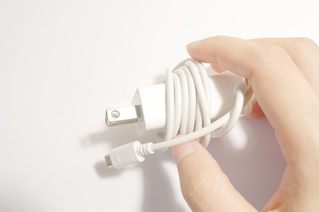 Photo cropped hand holding mobile phone charger over white background