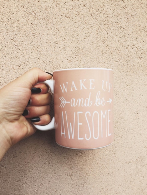 cropped hand holding mug against wall