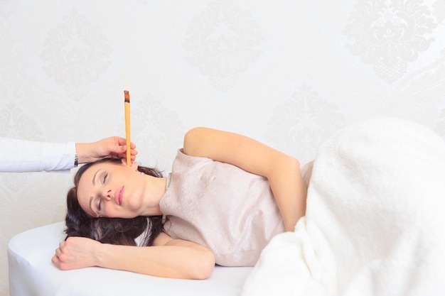 Cropped hand holding musical instrument in woman ear sleeping on bed