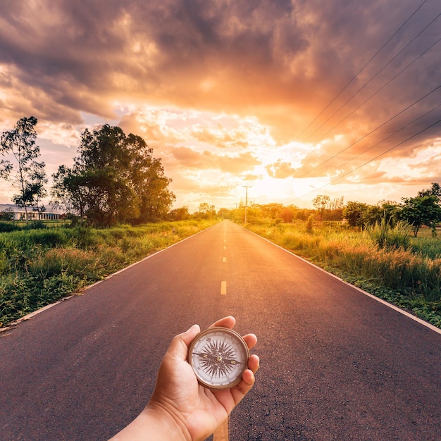 Foto mano tagliata che tiene la bussola di navigazione sulla strada durante il tramonto