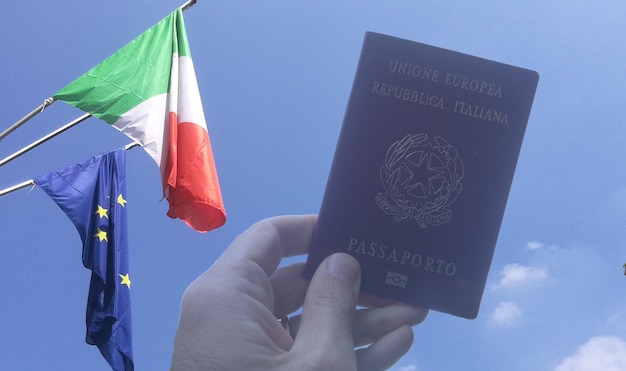 Foto mano tagliata che tiene il passaporto contro il cielo