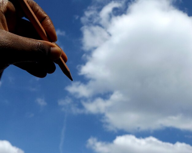 Foto mano tagliata che tiene una matita contro un cielo nuvoloso