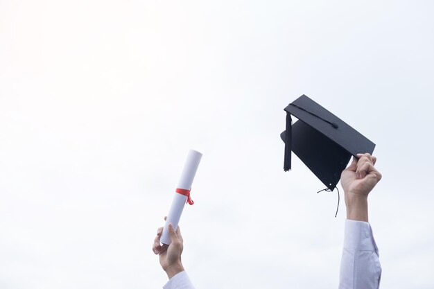 Photo cropped hand holding rolled certificate and mortarboard against clear sky