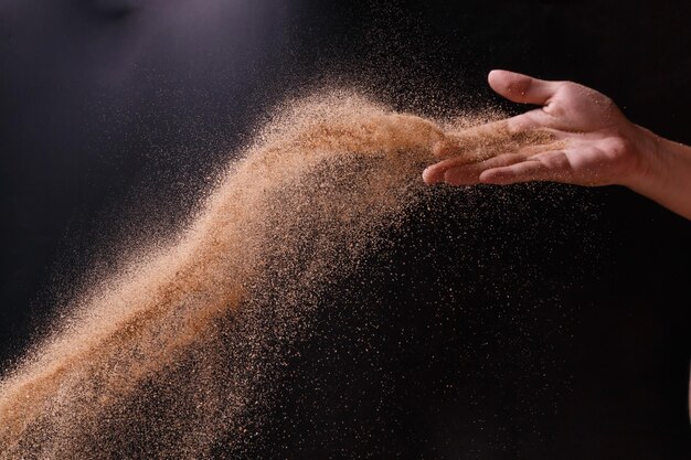 Foto mano tagliata che tiene la sabbia su uno sfondo nero