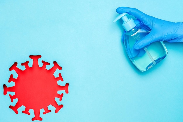 Photo cropped hand holding sanitizer over corona symbol against blue background