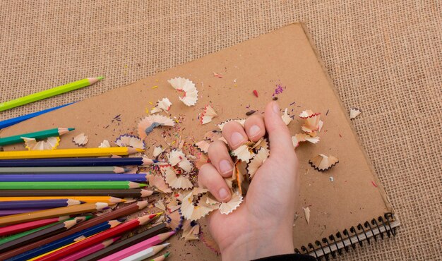 Photo cropped hand holding shavings with pencil and book on table