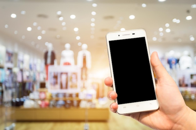 Foto mano tagliata che tiene uno smartphone in un centro commerciale