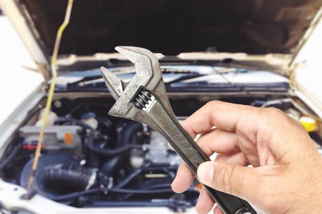 Cropped hand holding spanner against car at garage