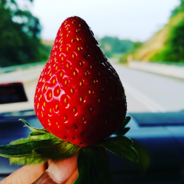 Foto mano tagliata che tiene una fragola in macchina