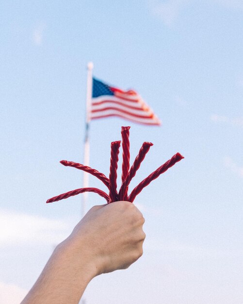 Foto mano tagliata che tiene la corda contro la bandiera americana