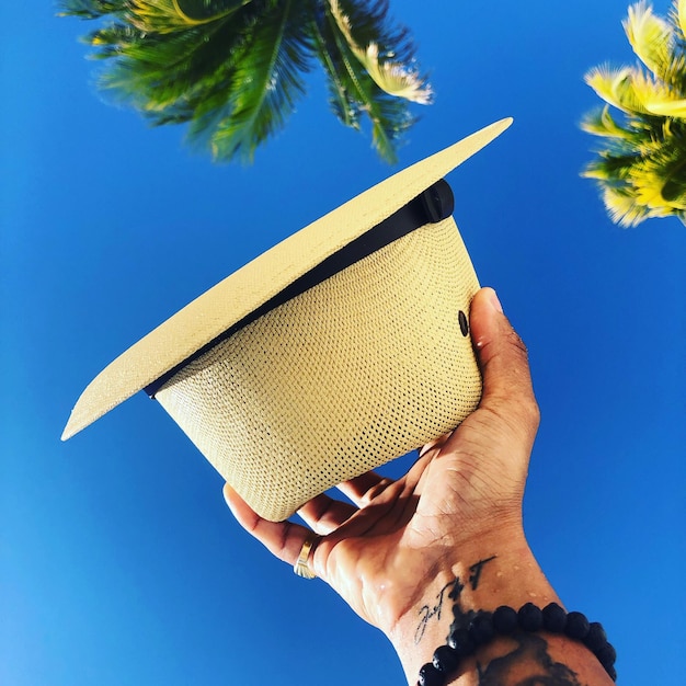 Photo cropped hand holding sun hat against clear blue sky