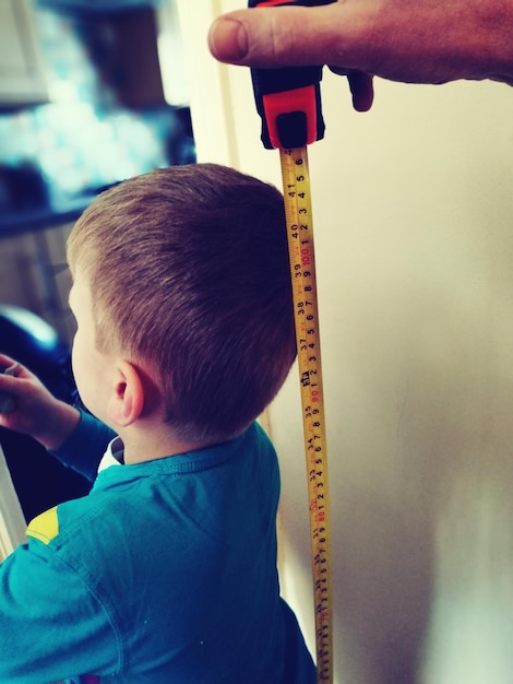 Photo cropped hand holding tape measure against boy at home