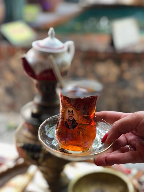 Photo cropped hand holding tea in glass on saucer