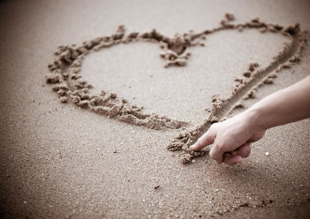 Фото Рука, сделанная в форме сердца на песке на пляже