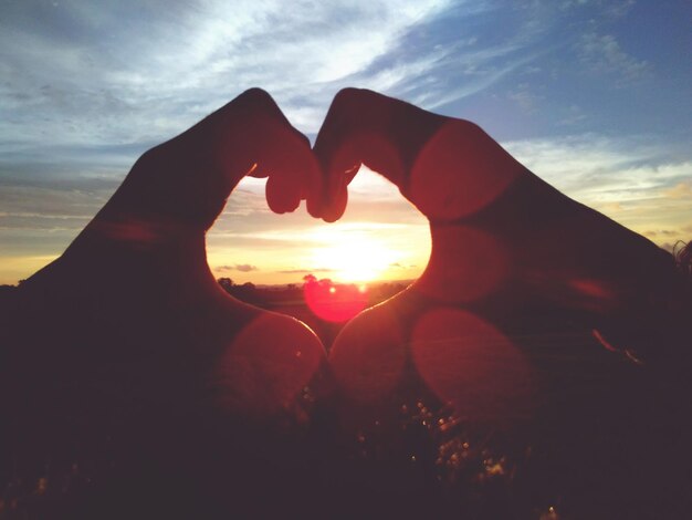 Foto mano tagliata che fa la forma di un cuore al tramonto