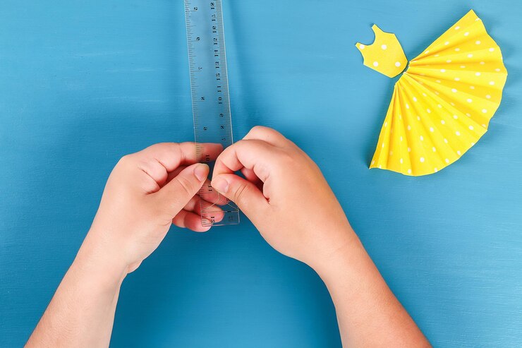 Cropped hand making small coathanger by paper dress over blue background