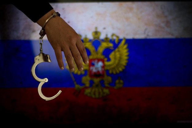 Photo cropped hand of male criminal with handcuffs against russian flag