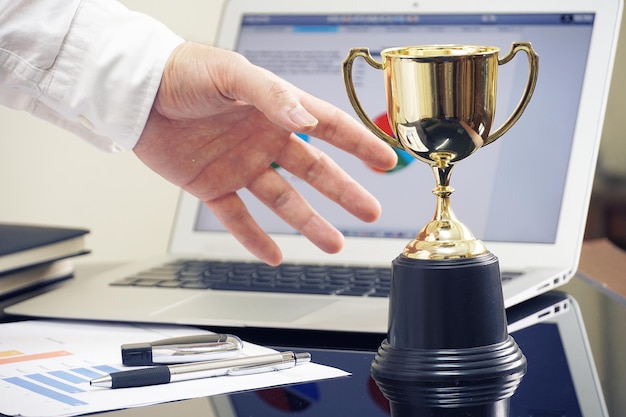 Foto la mano tagliata di un uomo con un trofeo e un portatile sul tavolo.