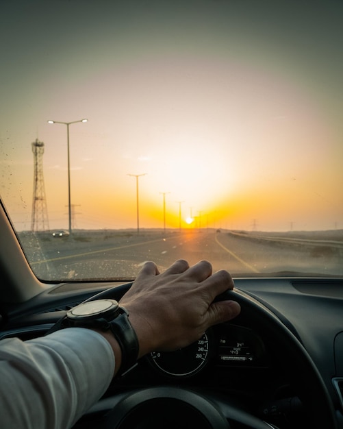 Cropped hand of man driving car on road during sunset