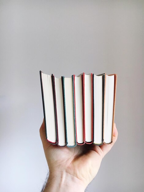 Foto mano tagliata di un uomo che tiene libri contro la parete