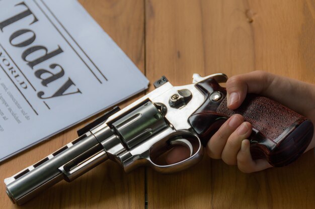 Photo cropped hand of man holding gun by newspaper on table