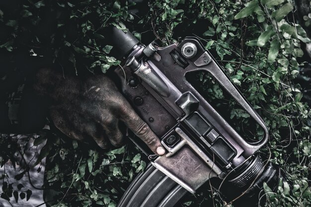 Foto mano tagliata di un uomo che tiene una pistola contro le piante