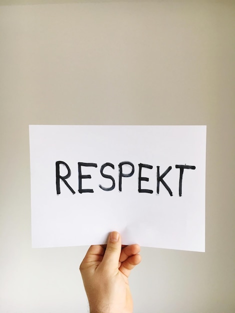 Photo cropped hand of man holding paper with text against wall