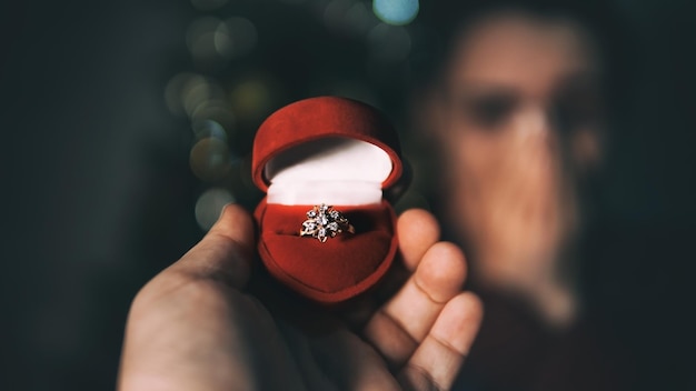 Foto mano tagliata di un uomo che tiene un anello in una scatola contro una donna sorpresa