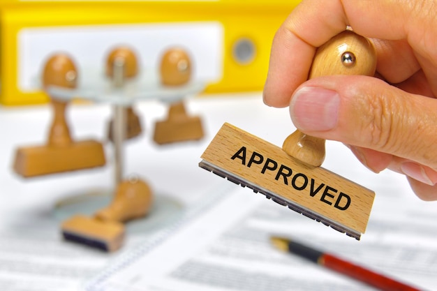 Photo cropped hand of man holding rubber stamp with approved text at desk