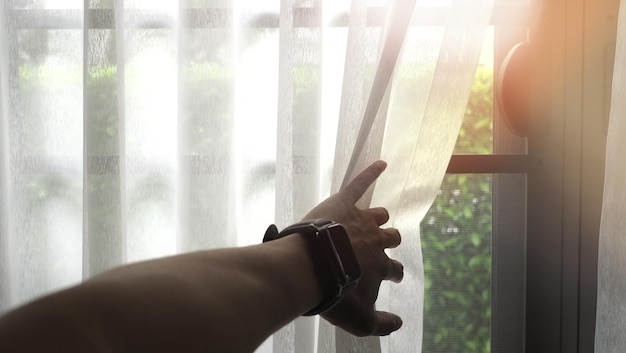 Photo cropped hand of man opening curtain against window at home