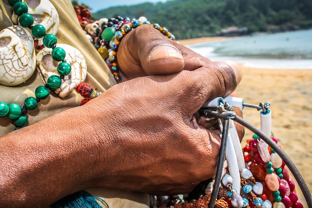 Foto mano tagliata di un uomo che vende collane di perle sulla spiaggia