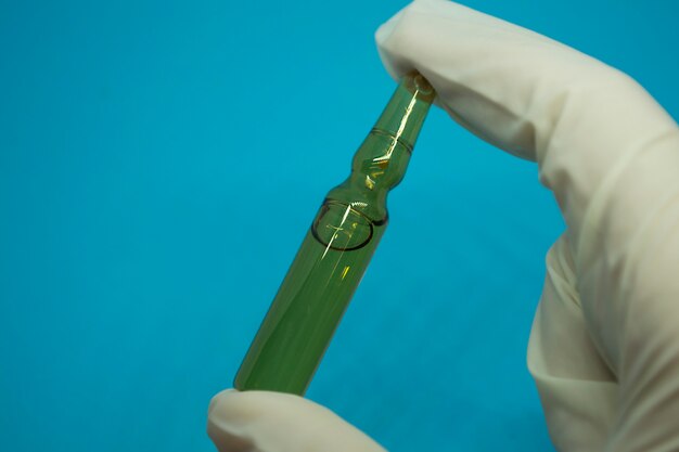 Cropped hand of man in white glove holding ampoule on blue background