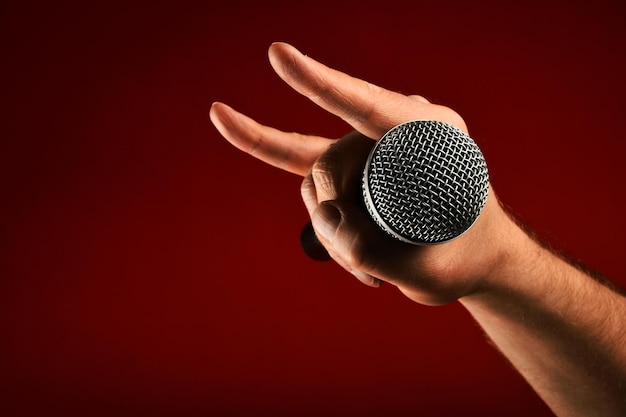 cropped hand of man with microphone while gesturing horn sign against maroon background
