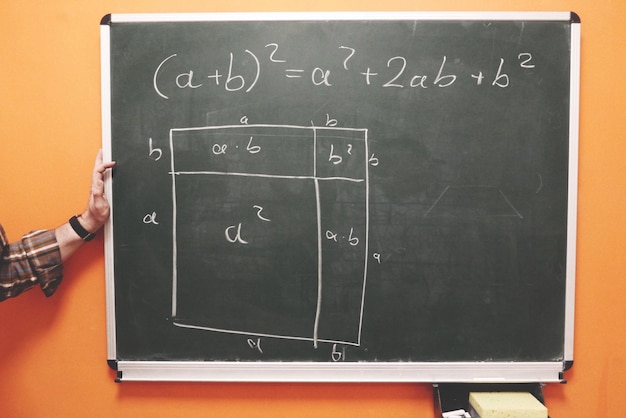 Foto mano tagliata del professore di matematica dalla lavagna contro la parete arancione