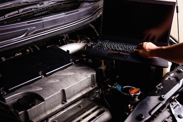 Cropped hand of mechanic using laptop while repairing car