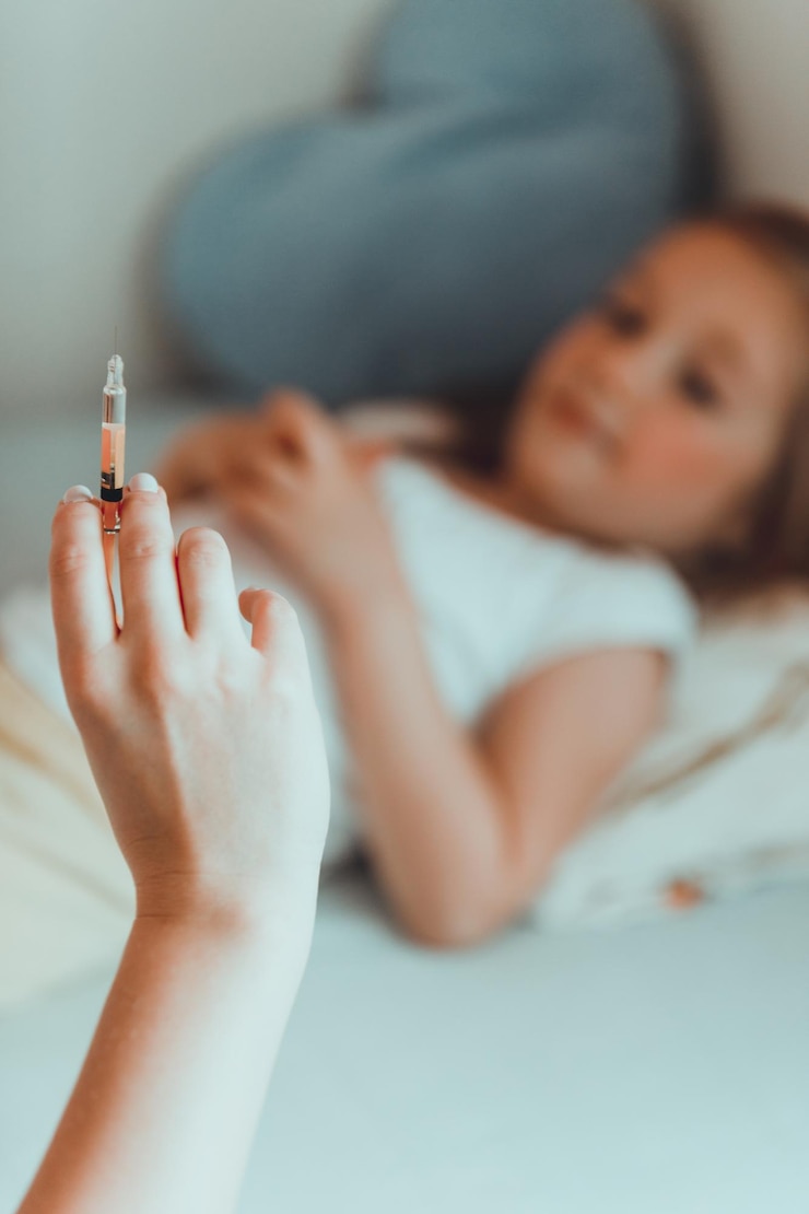 Photo cropped hand of mother holding syringe with daughter on bed at home