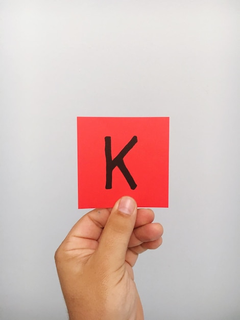 写真 灰色の背景に貼り付けられたメモの文字kを握っている人の手を切り取った