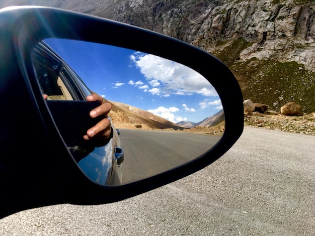 Фото Отрезанная рука человека, фотографирующего отражение в зеркале бокового вида автомобиля