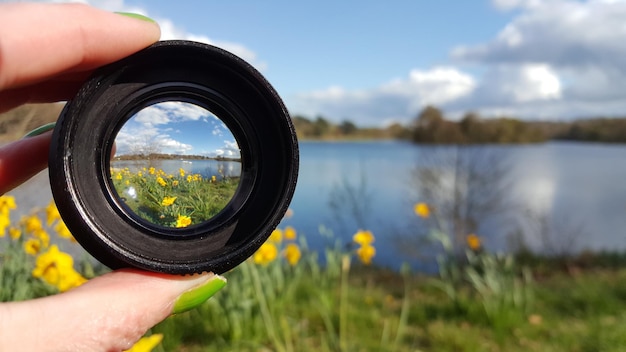 写真 黄色いナルシスと湖に照らしてレンズを握っている女性のカットされた手